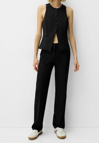 Svart ärmlös blazer med knappstängning, kombinerad med svarta vida byxor och vita sneakers, med enkla texturer och skräddarsydd design.