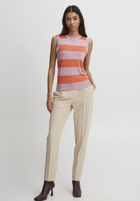 Top sin mangas con rayas alternas naranjas y rosa claro, combinado con pantalones beige acampanados y botas de tobillo marrón oscuro.