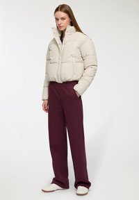 Beżowa, puchowa, krótką kurtka z wysokim kołnierzem i zapięciami na zatrzaski, zestawiona z bordowymi spodniami o szerokich nogawkach oraz białymi sneakersami. Gładka tekstura.