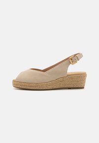 Sandalia de cuña de ante beige con punta abierta y plataforma de yute trenzado. Presenta un detalle de hebilla dorada en la correa del tobillo.