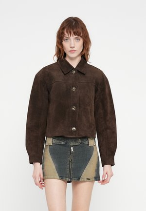 Veste en daim marron raccourcie avec de grands boutons, un col pointu et des épaules tombantes, associée à une jupe en denim multicolore avec une fermeture éclair centrale.
