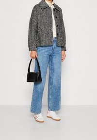 Czarna i biała marynarka w jodełkę, jasnobeżowy top, niebieskie szerokie spodnie dżinsowe, czarna torebka, białe buty z różowymi paskami, płaskie podeszwy.