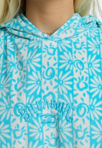 Toalla con capucha azul y blanca, con un patrón floral, textura suave y logo bordado de "Billabong" en el pecho.