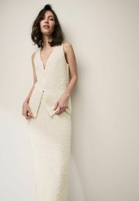 Robe tricotée avec un profond décolleté en V, de couleur crème douce. Le tissu texturé présente un motif complexe, avec une jupe ajustée.