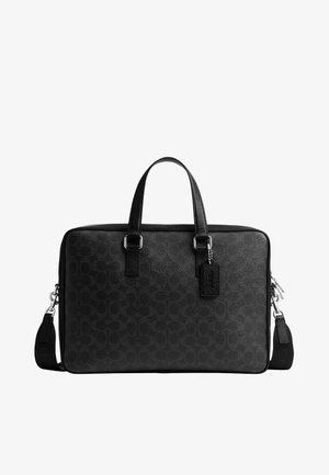 Serviette en cuir noir avec doubles poignées, bandoulière amovible, motif embossé subtil et petite étiquette suspendue.