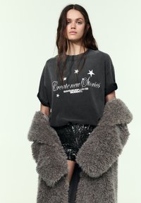 Mørkegrå oversized t-shirt med hvid tekst og stjernegrafik, kombineret med sorte palietshorts og en fluffy grå frakke.