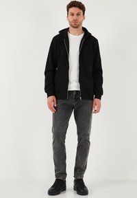 Černá mikina s kapucí na zip, s předními kapsami, doplněná šedými džínami a černými teniskami. Jednoduchý, ležérní design a střih.