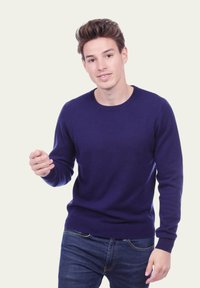 Pull en maille bleu marine à col rond et manches longues, tissu texturé, accompagné d'un jean bleu. Design simple et minimaliste.