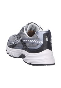 Sneaker Nike grigie e nere realizzate in materiali mesh e sintetici, con punta arrotondata, colletto imbottito, suola intermedia bianca e bande di accento sulla parte superiore.