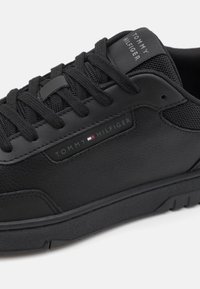 Svart lærsneakers med mesh-detaljer, og med svarte lisser og et Tommy Hilfiger-logo på siden. Slitesterk gummisåle.
