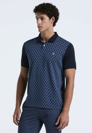 Marineblauwe polo met een geometrisch patroon in lichtblauw. Heeft korte mouwen, een klassieke kraag en een logo op de linkerborst.