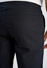 Granatowe spodnie z teksturowanej tkaniny, wyposażone w elastyczny pas i tylną kieszeń z widocznymi detalami szwu.