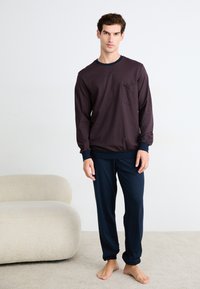 Haut à manches longues bordeaux avec un motif géométrique et une poche, associé à un pantalon bleu marine. Tissu doux, coupe décontractée, poignets et taille élastiques.