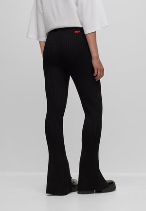 Černé žebrované legíny s rozšířenými nohavicemi a vysokým pasem, s malou červenou značkou vzadu a hladkou, pružnou texturou.
