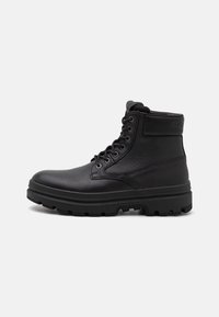 Stivaletto in pelle nera con finitura texturizzata, punta rotonda, sei occhielli e suola robusta. Presenta un collo imbottito e un logo discreto.