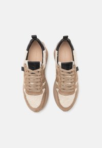 Zapatillas en tonos beige y crema con un upper texturizado, que cuentan con cordones, un tirador negro en el talón y una suela acolchada.