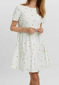 Robe blanche à manches courtes avec un ourlet en couches, ornée de petits motifs de fleurs jaunes, fabriquée en tissu léger.