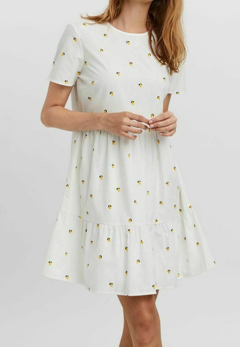 Robe blanche à manches courtes avec un ourlet en couches, ornée de petits motifs de fleurs jaunes, fabriquée en tissu léger.