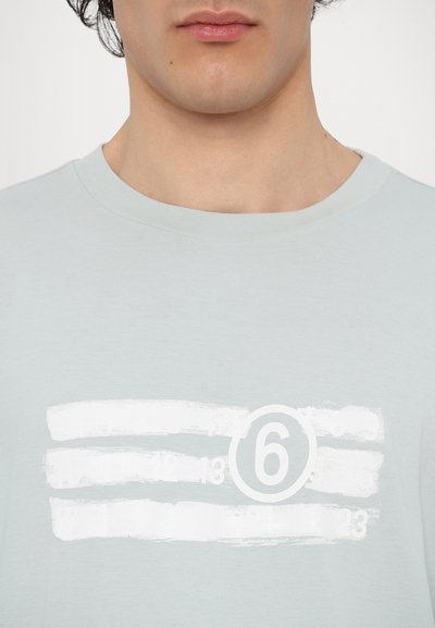 Γαλάζιο μπλουζάκι με στρογγυλή λαιμόκοψη και κοντά μανίκια, με λευκή γραφική παράσταση οριζόντιων γραμμών και τον αριθμό "6" μέσα σε έναν κύκλο.