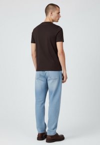 Czarny t-shirt z krótkim rękawem, luźny krój, materiał bawełniany. Noszony z jasnoniebieskimi dżinsami, posiadającymi tylne kieszenie i prostą nogawkę.