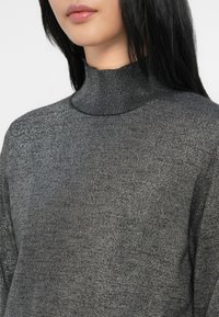 Suéter de gola alta em malha cinza escuro com uma textura ligeiramente brilhante, apresentando um design justo.