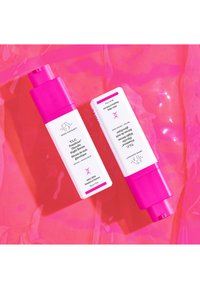 Two skincare bottles on a pink background: one with a pink pump top and white body, the other is white with a pink accent. Both feature text labels.