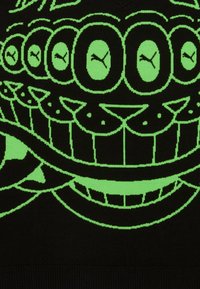 Suéter negro con un gran patrón gráfico en verde de ojos y una boca. El diseño incluye detalles estilizados y formas redondeadas.