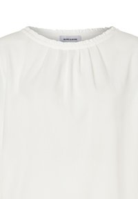 Biała bluzka z okrągłym, marszczonym dekoltem i falbanowym wykończeniem. Wykonana z lekkiego materiału o gładkiej fakturze. Widoczna metka marki.