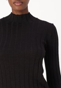 Maglione nero a collo alto a coste con strisce verticali, un collo alto e maniche lunghe in un morbido tessuto testurizzato.