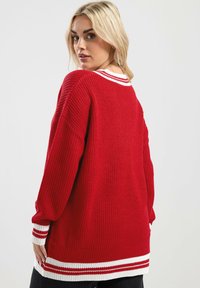 Czerwona sweter z dzianiny z prążkowaną teksturą, szerokimi rękawami i białymi paskami na dekolcie oraz u dołu.