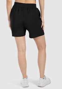 Pantalones cortos negros con una cinturilla elástica alta, textura suave y bolsillos laterales, combinados con zapatillas deportivas blancas.