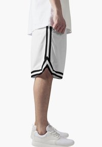 Shorts de sport blancs avec des accents noirs, dotés d'une texture en maille et de rayures sur les côtés. Associés à des baskets blanches.