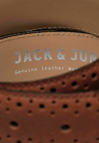 Unutra smeškanih smešnih smešnih isključivo brenda "JACK & JON" i "Prava koža" na svetlo bež pozadini.
