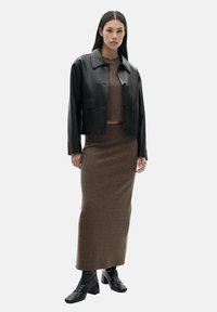 Veste en cuir noir courte sur un haut en maille marron et une jupe longue assortie. Modèle portant des bottines noires. Fond gris uni.