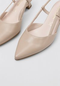 Tacones slingback de piel beige con punta afilada y tacón bajo tipo bloque. Presentan un diseño con corte y una textura suave.