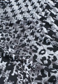 Schwarzes und weißes Gewebe mit einem abwechslungsreichen abstrakten Muster, das unregelmäßige Formen und Texturen zeigt und eine Mischung aus glatten und matten Oberflächen aufweist.