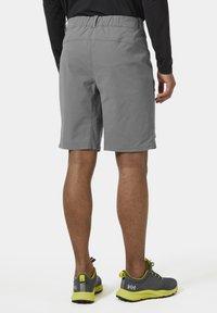 Šedé kraťasy s elastickým pasem, vyrobené z lehkého materiálu a s přiléhavým střihem. Nosené se šedými a neonově žlutými botami.