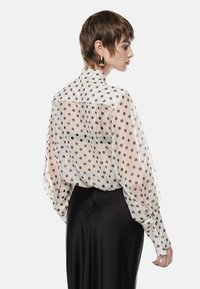 Blusa trasparente a pois con maniche a palloncino, polsini con bottoni e colletto alto in crema e nero. Abbinata a una gonna nera liscia.