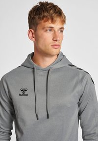 Grijze hoodie met een zachte textuur, voorzien van een trekkoord, zwart logo en accenten op de zijpanelen. Eenvoudig ontwerp met een relaxed fit.
