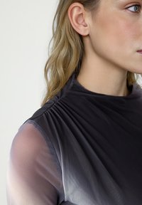 Czarny szary top z wysokim dekoltem, z przezroczystymi bufiastymi rękawami i marszczeniem na ramionach. Gładka faktura, minimalny design.