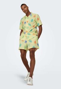 Camisa de manga corta con cuello y pantalones cortos a juego en amarillo claro, con estampados coloridos de temática marina, que presentan una tela texturizada y un corte holgado.