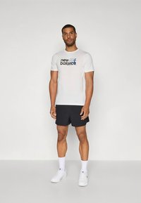 Valge puuvillane T-särk tekstiga "new balance", mustade lühikeste pükstega. Modell kannab valgeid spordijalatseid ja valgeid pahkluu sokke.