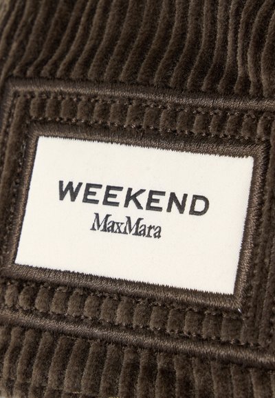 Étiquette en tissu blanc avec texte noir "WEEKEND MaxMara" cousue sur un tissu en velours côtelé marron foncé.