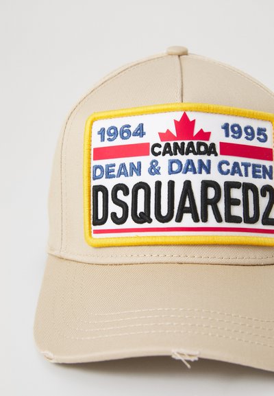 Casquette de baseball beige avec un patch à l'avant représentant une feuille d'érable rouge, du texte en bleu et noir, bordé de rayures jaunes et rouges.