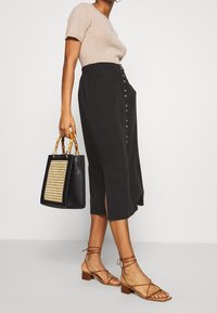 Černá plisovaná midi sukně s předními knoflíky, spárovaná s béžovým topem s krátkým rukávem, hnědými sandály na průvleky a černou taškou s tkaným vzorem.