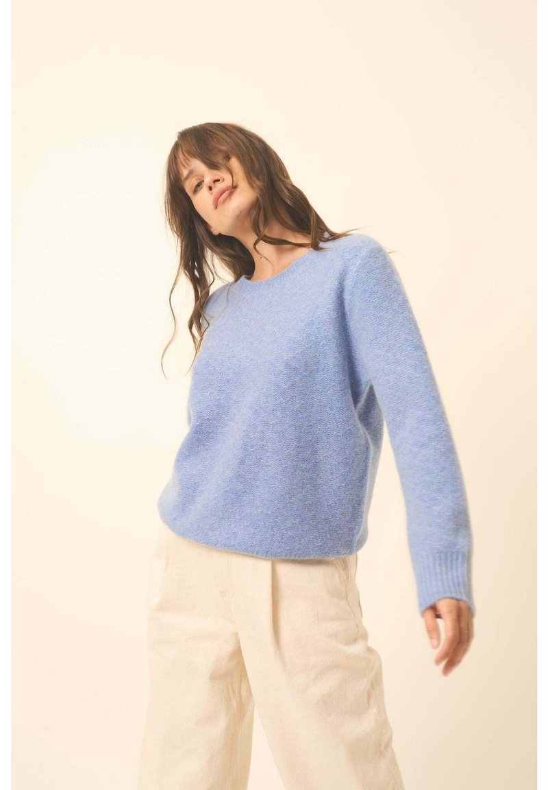 Hellblau gestrickter Pullover mit rundem Halsausschnitt und langen Ärmeln, kombiniert mit cremefarbenen, weit geschnittenen Hosen. Strukturierter Stoff, lockere Passform.