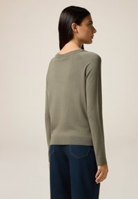 Olivgrüner Pullover mit geripptem Saum und Bündchen, figurnaher Schnitt, langen Ärmeln und rundem Ausschnitt, kombiniert mit dunkelblauen weit geschnittenen Jeans.