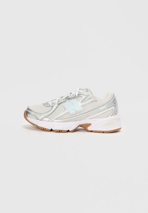 Chaussure de course légère avec une tige en mesh argentée et blanche, des accents bleus, une semelle rembourrée et une semelle extérieure en caoutchouc texturé marron.
