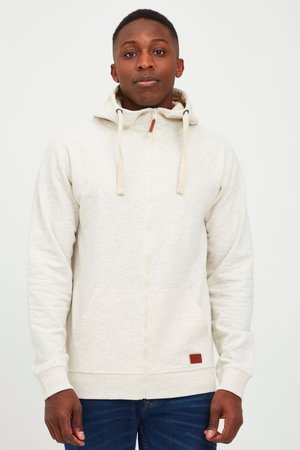Lichtbeige rits-hoodie met een voorzak en een capuchon met trekkoord, voorzien van een bruine leren patch aan de onderrand en geribbelde manchetten.