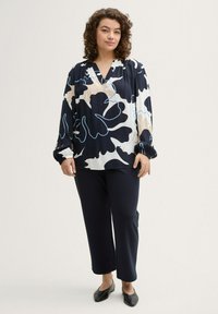 Bluse mit Blumenmuster in Marineblau, Creme und Hellblau, mit entspannter Passform, langen Ärmeln und V-Ausschnitt. Kombiniert mit dunkelblauen Hosen.